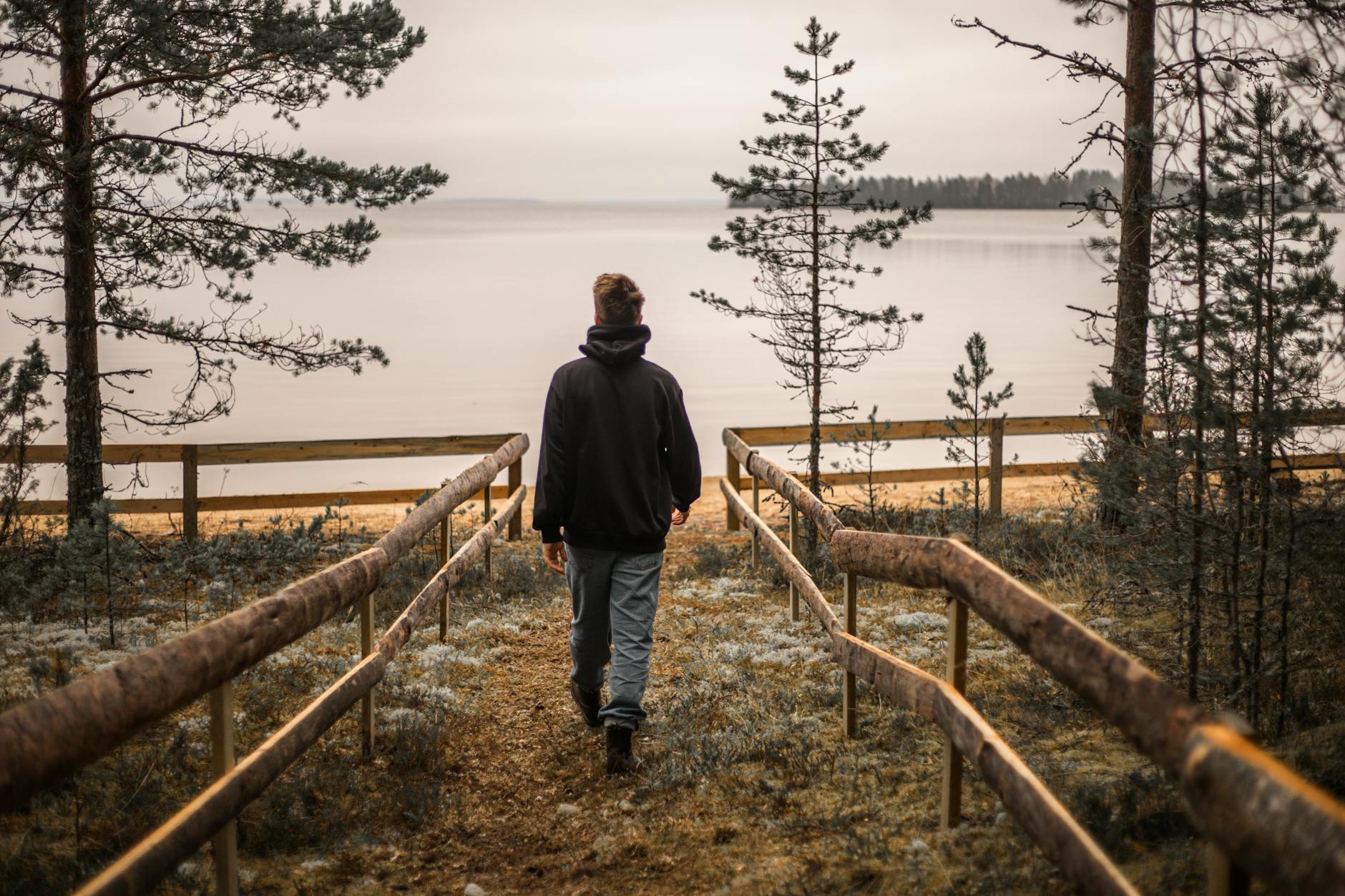 a person in black jacket walking on the pathway beside the beach